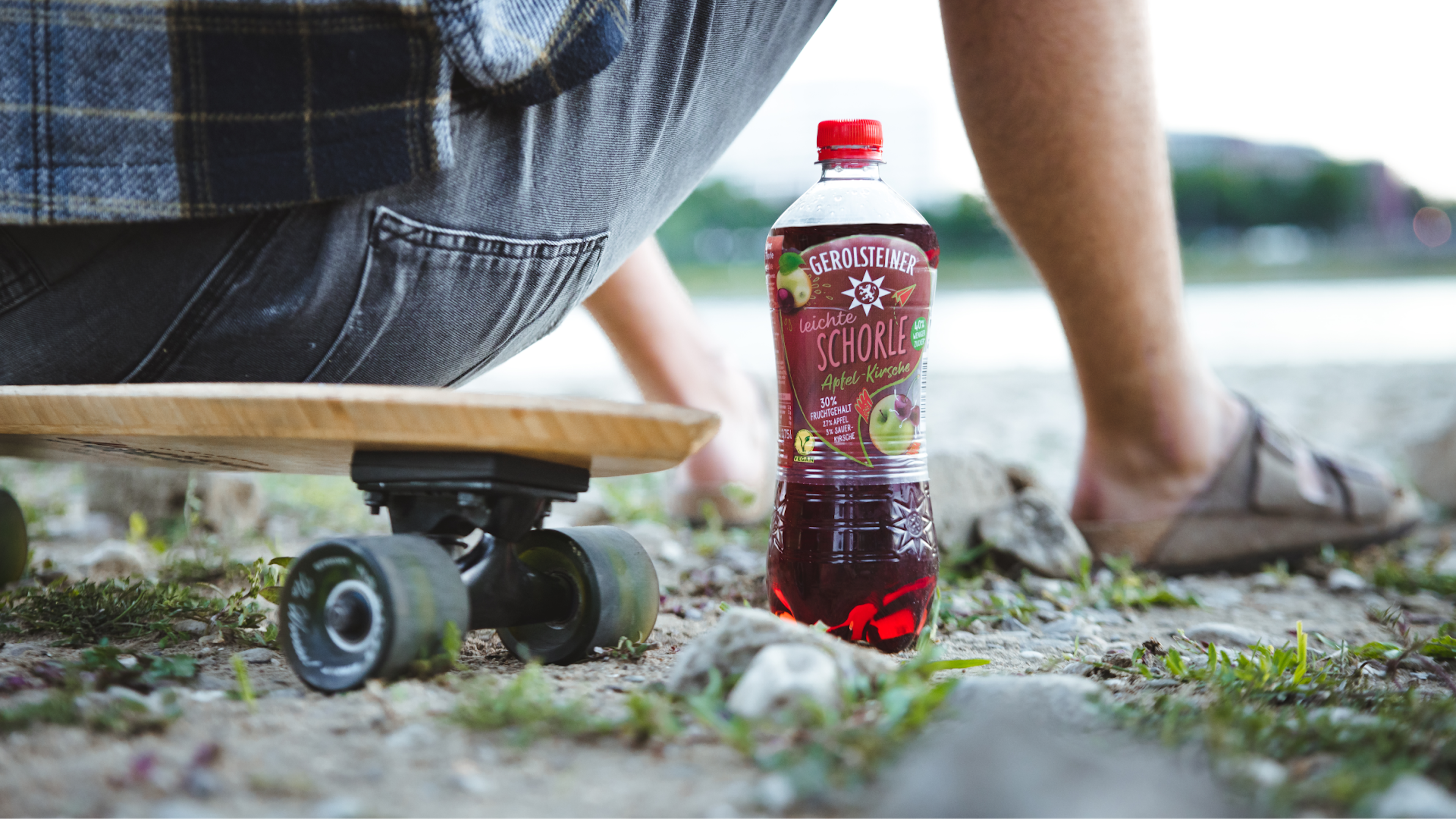 Eine nahe Bodenaufnahme einer Flasche Apfel-Kirsch-Schorle neben einem Skateboard und Füßen eines Skateboarders.
