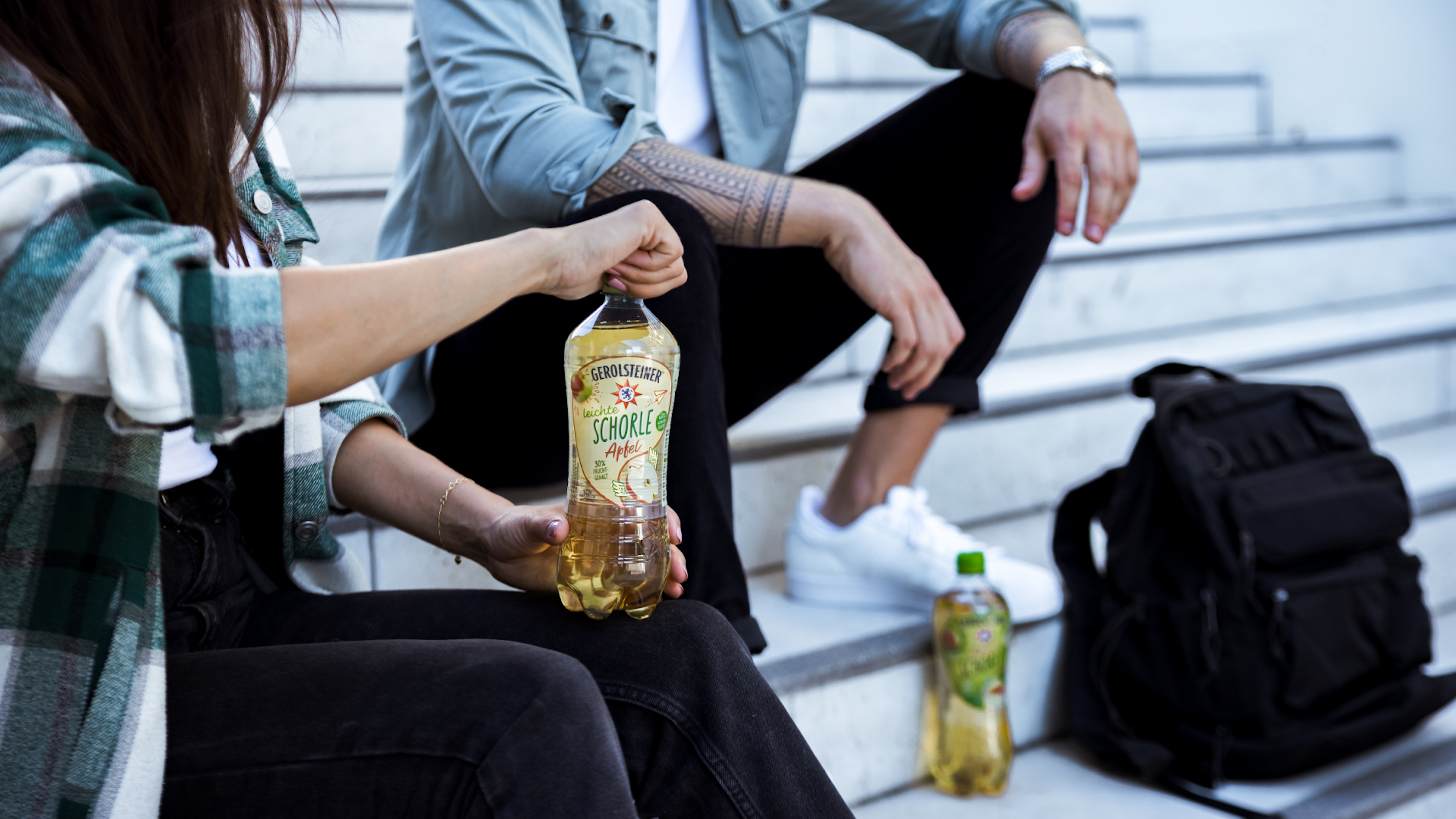 Zwei Personen sitzen auf Stufen und teilen sich eine Flasche Leichte Apfelschorle.