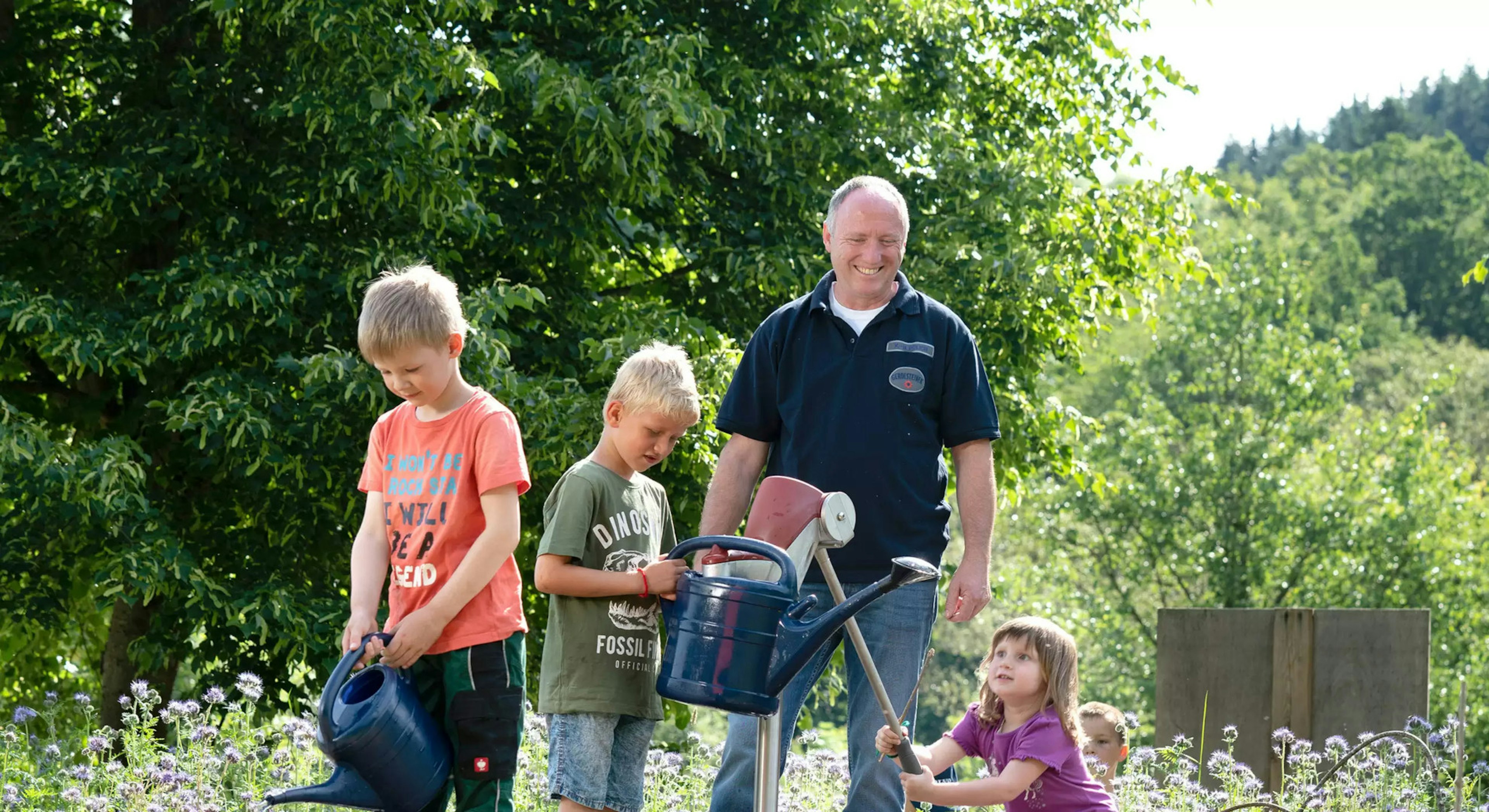 Ein Mann mit Gerolsteiner Dienstkleidung mit drei Kindern bei der Gartenarbeit