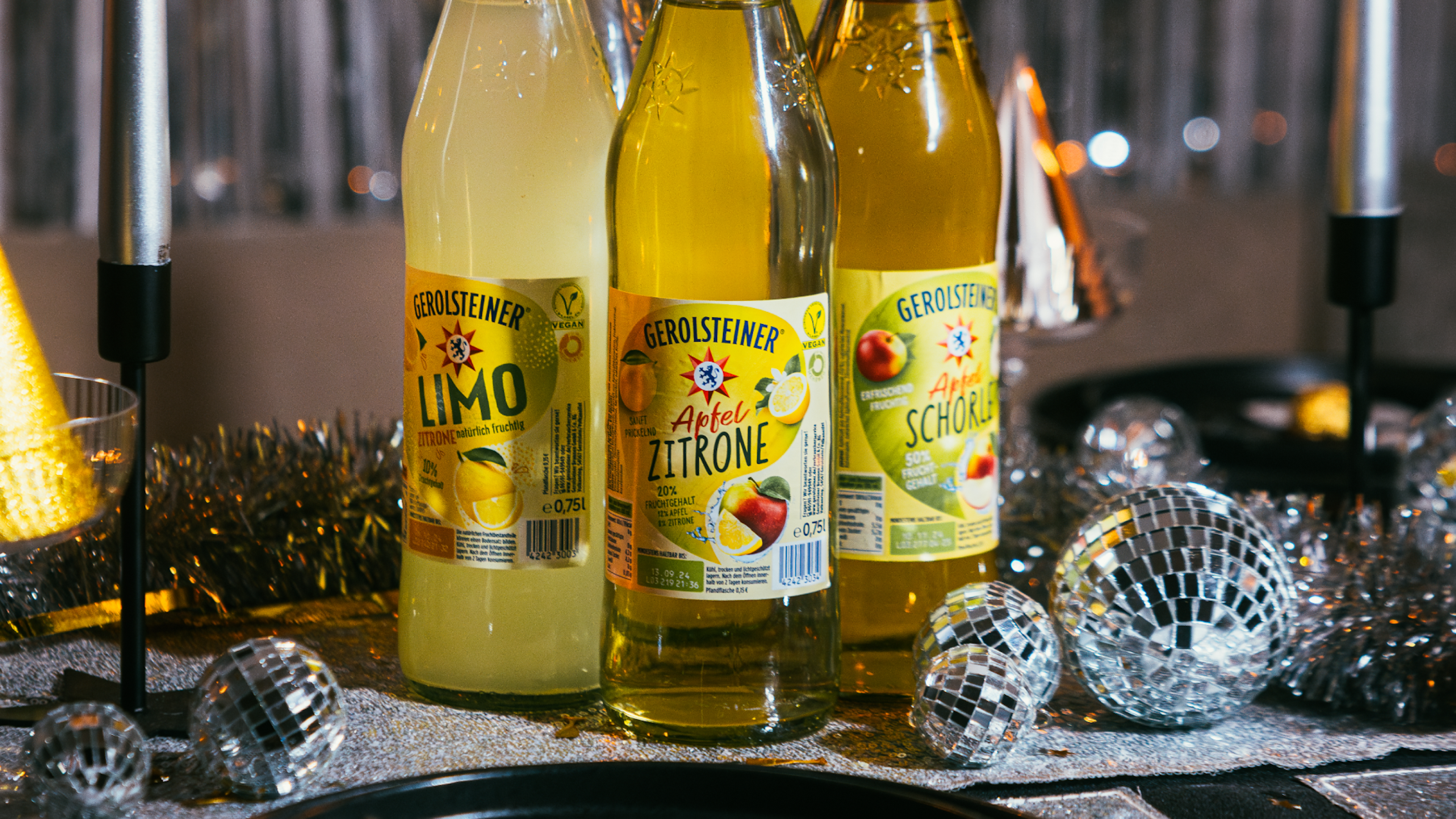 Flaschen von Apfel-Zitrone-Getränken stehen auf einem festlichen Tisch mit Disco-Kugeln.