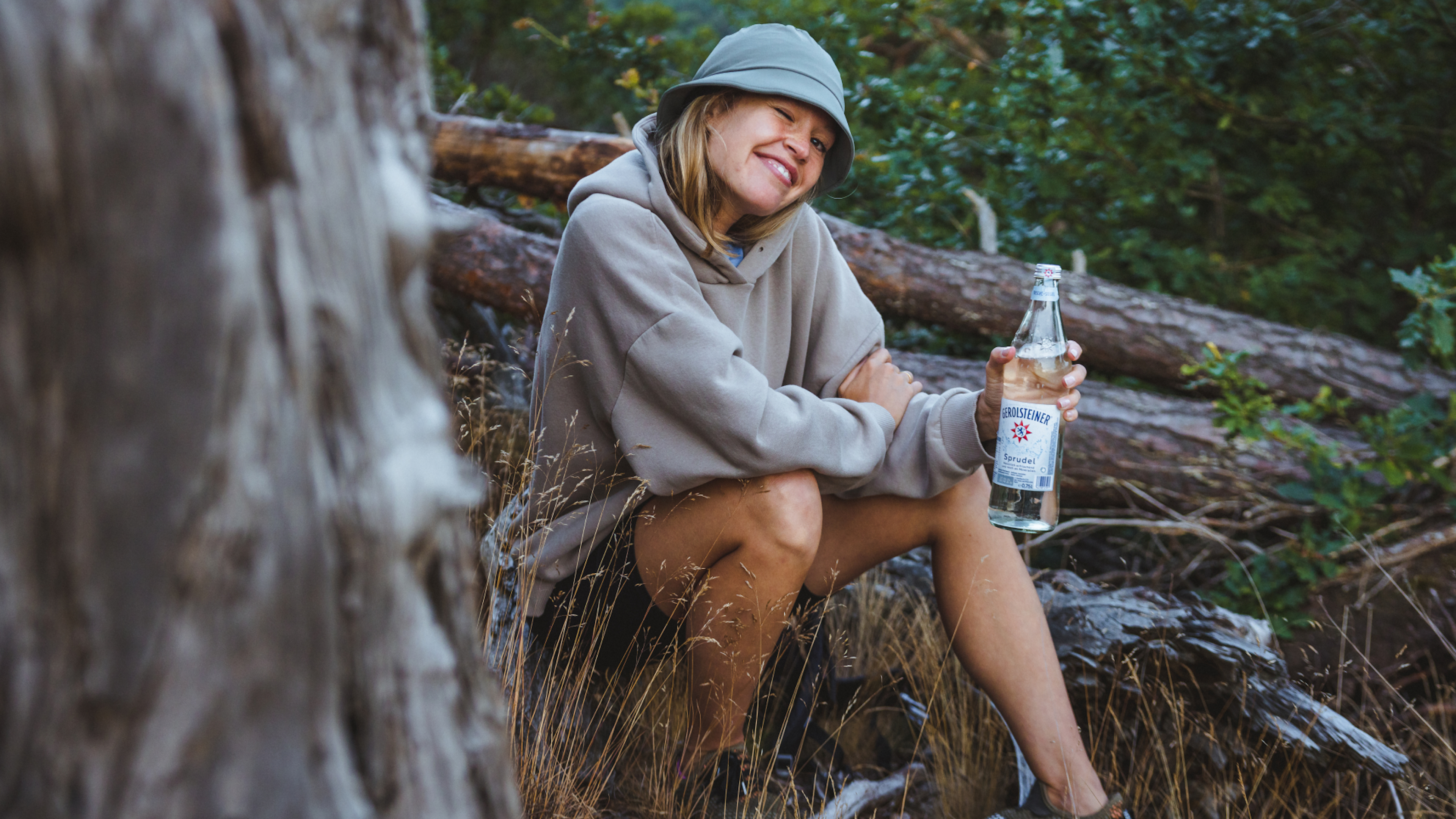 Frau sitzt auf einem Baumstamm mit einer Flasche in der Hand