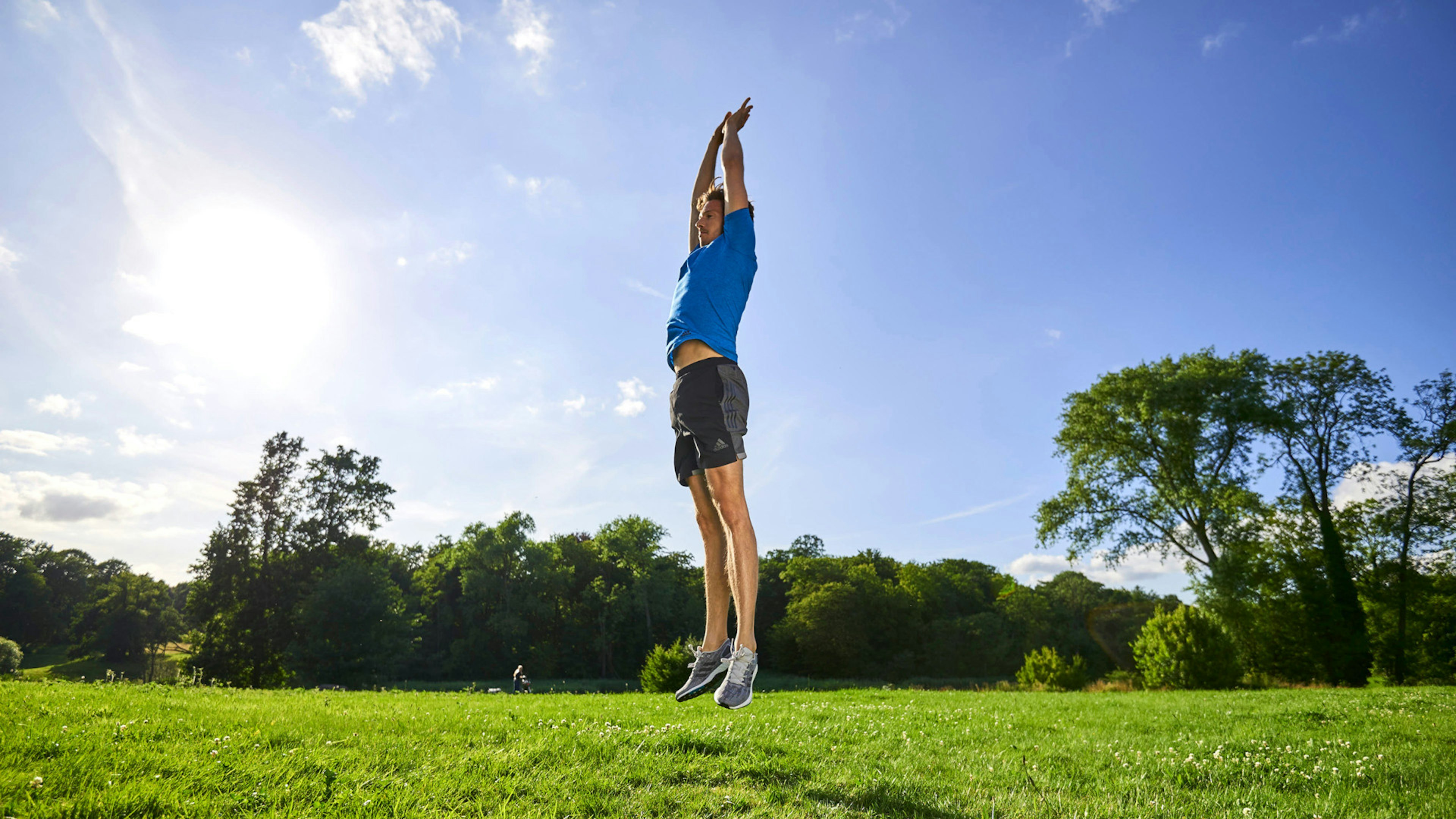 Ein Mann in Sportkleidung der auf einer grünen Füße mit den Armen gen Himmel nach oben springt.